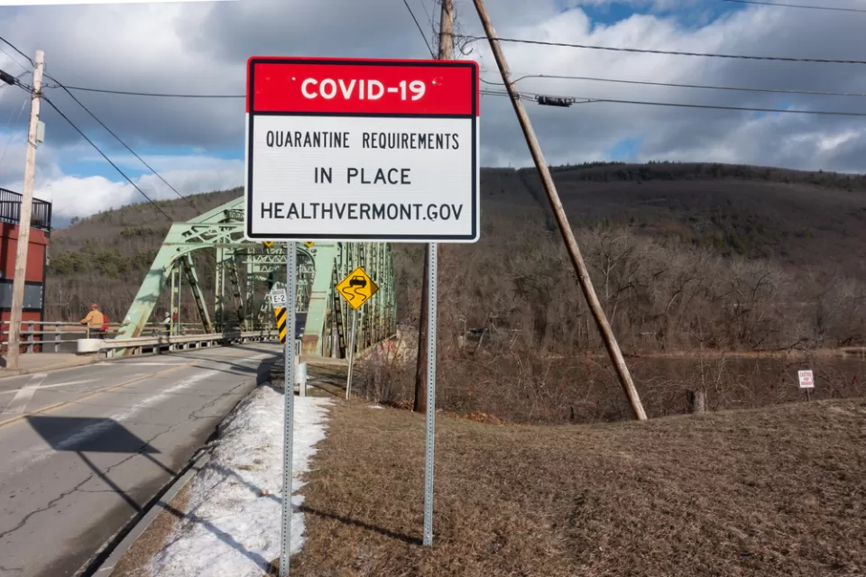 An image of a bridge in Vermont with a sign in front of it announcing a COVID-19 quarantine order.